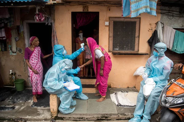 MUMBAI/INDIA- JUNE 17, 2020: Health workers wearing protective gear monitor body temperature of people at the COVID health check up camp at Ramabai colony slum during the COVID-19 Coronavirus pandemic.