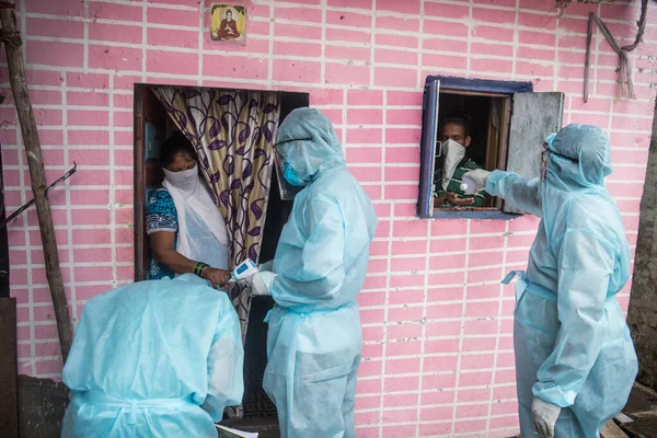 MUMBAI/INDIA- JUNE 17, 2020: Health workers wearing protective gear monitor body temperature of people at the COVID health check up camp at Ramabai colony slum during the COVID-19 Coronavirus pandemic.