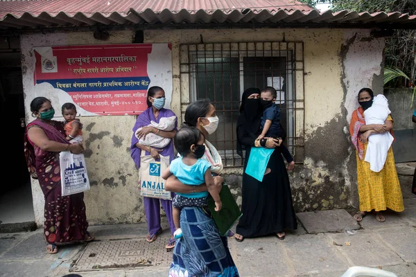 MUMBAI / INDIA - 23 Haziran 2020: COVID-19 Coronavirus salgını sırasında Dharvai gecekondu mahallesinde bir halk sağlık merkezinde yapılan ulusal immünasyon programı sırasında çocuk aşısı almak için maske giyen insanlar kuyrukta bekliyor.