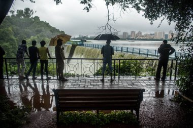 MUMBAI / INDIA - 16 Temmuz 2020: Bombay 'da sağanak yağış sonrasında Powai Gölü' nden taşan suyun önünde insanlar şemsiyeyle ayakta duruyor.