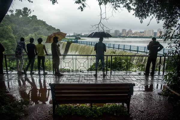 MUMBAI / INDIA - 16 Temmuz 2020: Bombay 'da sağanak yağış sonrasında Powai Gölü' nden taşan suyun önünde insanlar şemsiyeyle ayakta duruyor.