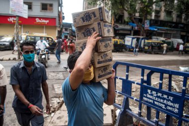 MUMBAI / INDIA - 3 AĞUSTOS 2020: COVID-19 Coronavirus salgınının yoğun saatinde Dharavi varoşlarında yüz maskesi takan bir işçi kutuları taşır.