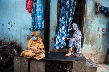 MUMBAI / INDIA - 3 AĞUSTOS 2020: Yüz maskesi takan yaşlı kadınlar COVID-19 Coronavirus salgını sırasında Dharavi varoşlarındaki evinin önünde oturuyorlar.