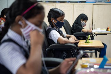 MUMBAI / INDIA - 27 Ekim 2020: Covid-19 Coronavirus salgını sırasında Mumbai 'deki Imamwada' da Online Education Mobile Library 'nin bir parçası olarak ders sırasında cep telefonlarında yüz maskesi takan öğrenciler