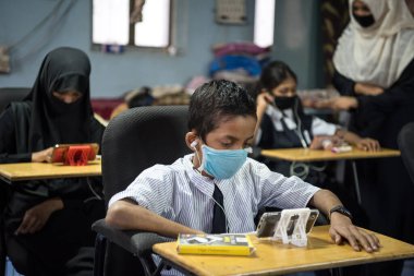 MUMBAI / INDIA - 27 Ekim 2020: Covid-19 Coronavirus salgını sırasında Mumbai 'deki Imamwada' da Online Education Mobile Library 'nin bir parçası olarak ders sırasında cep telefonlarında yüz maskesi takan öğrenciler
