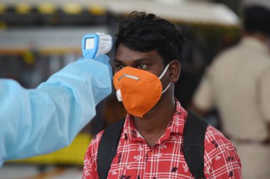 MUMBAI-INDIA - 27 Kasım 2020: Bir sağlık çalışanı, koronavirüsün yayılmasına karşı önleyici bir önlem olarak Bandra terminalindeki bir yolcunun sıcaklığını kontrol eder.