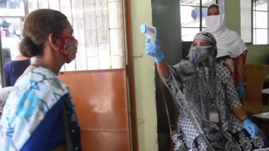 MUMBAI / INDIA - 29 Nisan 2020: COVID-19 Coronavirus 'a karşı önleyici bir önlem olarak Dadar' da bir kadının vücut sıcaklığını izleyen sağlık çalışanı.