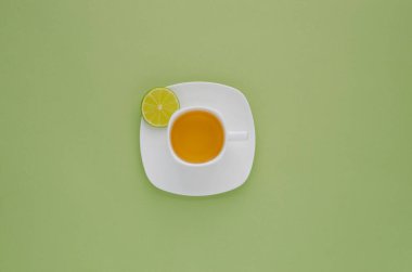 Yeşil pastel arka planda limonlu bir fincanda demlenmiş yeşil çay. en üstteki görünüm.