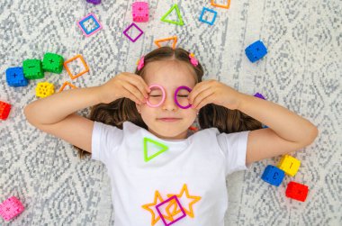 Şirin küçük kız renkli figürlerle oynuyor. Gülümseyen çocuk