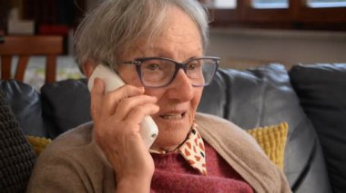 Ön plandaki etkileyici yaşlı bayan telefonda bir arkadaşıyla konuşuyor.