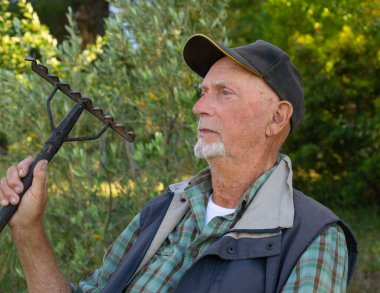 Şapkası ve tırmığı olan yaşlı Tuscan çiftçisi tarlasında dinleniyor.