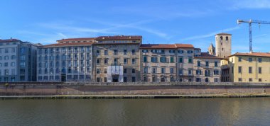 Pisa 'nın Lungarno Antonio Pacinotti' si Arno Nehri 'ni çevreleyen tarihi binaların manzarası. Canlı şehir manzarası Rönesans cazibesiyle günlük yaşamı harmanlıyor, parlak mavi Toskana gökyüzü altında.