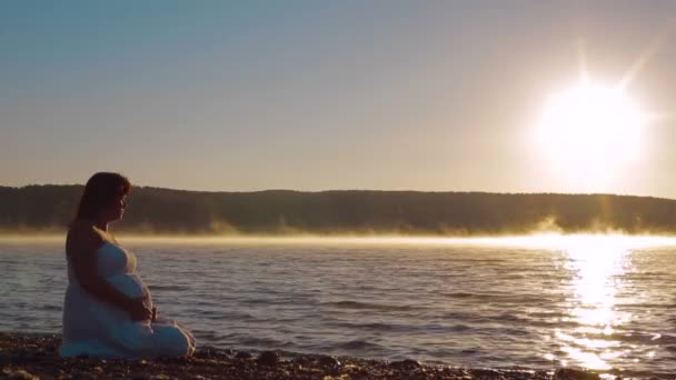 Gravida sitter på sjön i den tidiga morgonen och titta på soluppgången. — Stockvideo
