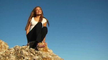 Kız kayanın üzerinde oturuyor.