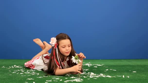Kız 6 yaşındaki eski çim üzerinde yalan ve papatya yaprakları ayırır. — Stok video