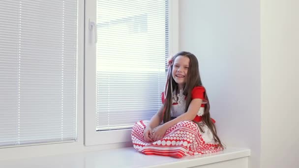 Dívka sedí v okně a sledujte, co se děje na ulici 6-7 let. — Stock video