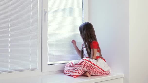 Das Mädchen ist traurig am Fenster im Zimmer. — Stockvideo