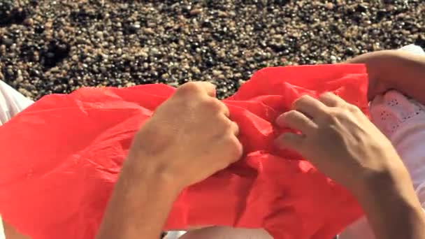 L'homme et la femme ouvrent un paquet rouge assis sur la plage — Video