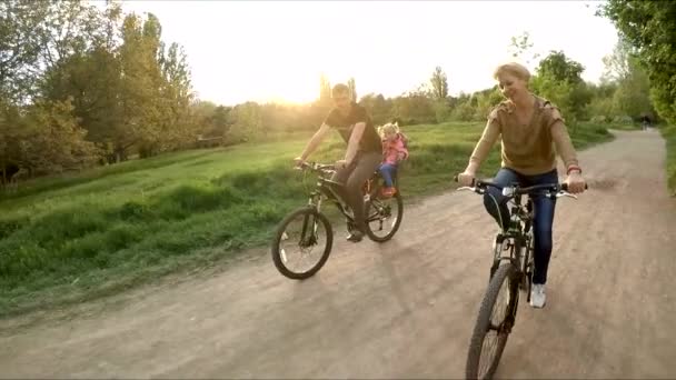 Молодая счастливая семья ездит на велосипедах в зеленом парке — стоковое видео