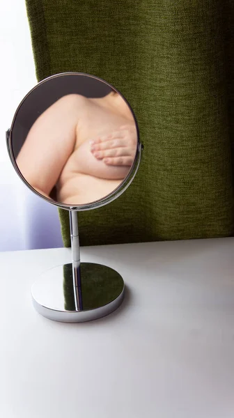 一个胖女人的形象反映在一个圆形的镜子里 镜子站在一张白色的桌子上 背景是绿色的窗帘 — 图库照片