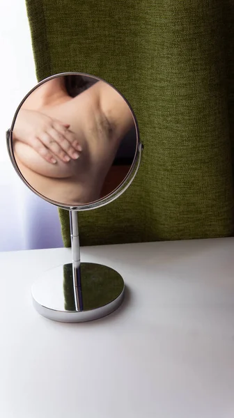 一个胖女人的形象反映在一个圆形的镜子里 镜子站在一张白色的桌子上 背景是绿色的窗帘 — 图库照片