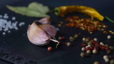 Taş tabakta baharatlar. Siyah arka plan. Siyah taş. Sarımsak, deniz tuzu, biber, acı biber, defne yaprağı.