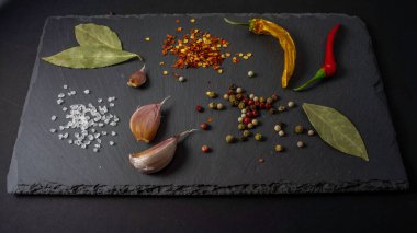Taş tabakta baharatlar. Siyah arka plan. Siyah taş. Sarımsak, deniz tuzu, biber, acı biber, defne yaprağı.