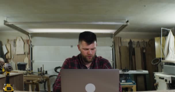 En europeisk man som talar med videosamtal på en bärbar dator i en snickarverkstad — Stockvideo