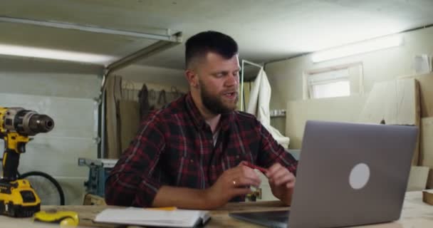 大工の工房でノートパソコンでビデオ通話をしているヨーロッパ人の男性が — ストック動画