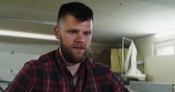 Um homem europeu falando por videochamada em um laptop em uma oficina de carpintaria — Vídeo de Stock