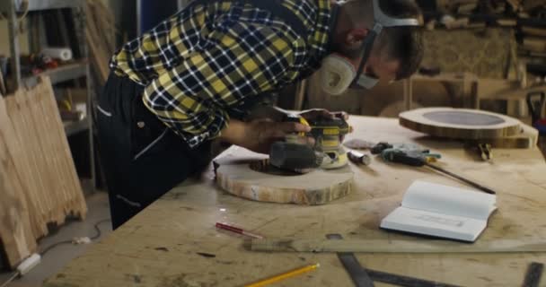 Man med europeiskt utseende i skyddande hörlurar och en mask bearbetar ett trä — Stockvideo