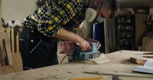 Muž evropského vzhledu v ochranných sluchátkách a masce zpracovává dřevo — Stock video
