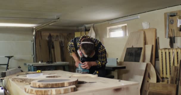Mann europäischen Aussehens mit schützenden Kopfhörern und Maske bearbeitet Holz — Stockvideo