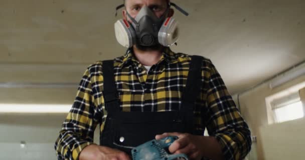 Человек в защитной маске с деревообрабатывающим инструментом смотрит в камеру — стоковое видео