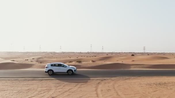 Vertikales Schwenken von einem Quadrocopter aus. Weißes Auto fährt auf Straße in der Wüste — Stockvideo