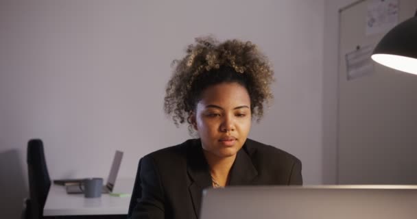 Ragazza africana in giacca e cravatta guarda schermo del computer portatile in ufficio alla luce della lampada — Video Stock