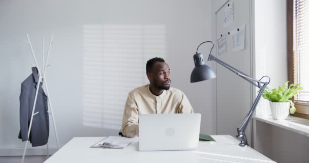 Zwart guy met een baard werkt in een modern kantoor raakt zijn gezicht met zijn handen — Stockvideo