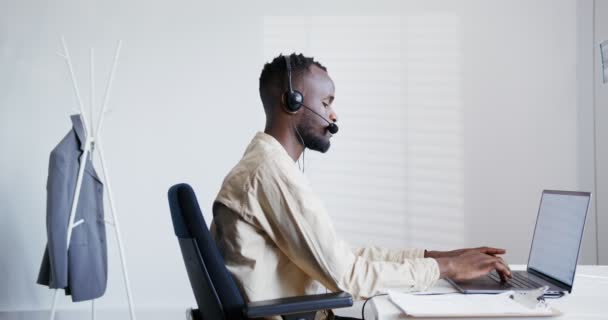 Чорний хлопець з бородою говорить в мікрофон навушників і друкує — стокове відео