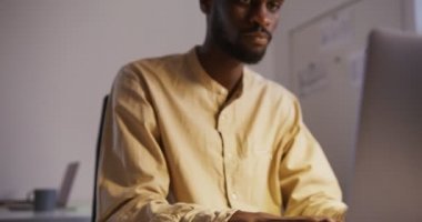 : Ofisteki dizüstü bilgisayarda masa lambasının altında yazan siyahi bir adam.