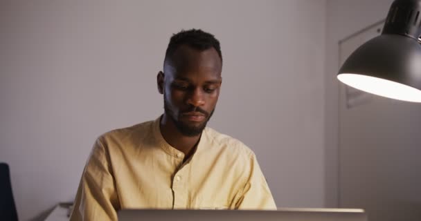 Noir guy tapant sur un ordinateur portable dans un bureau sous la lumière de la lampe de table — Video