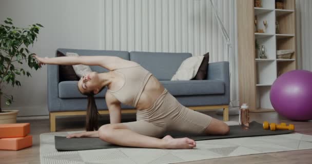 Fille européenne vêtue de vêtements de sport faire des courbes tout en étant assis en demi-fentes — Video