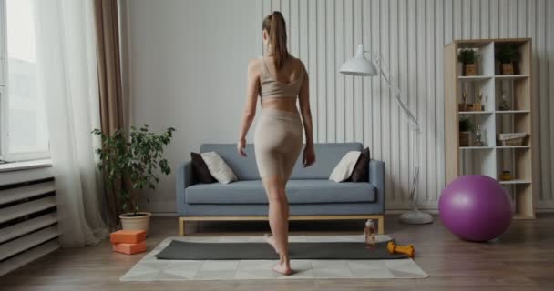 Spor giyimli Avrupalı bir kız gelir ve jimnastik halısında lotus pozisyonunda oturur. — Stok video