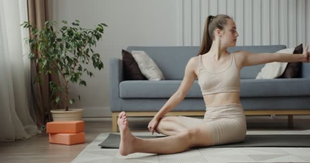 Spor kıyafetleri giymiş Avrupalı bir kız jimnastik minderinde oturarak egzersiz yapıyor. — Stok video