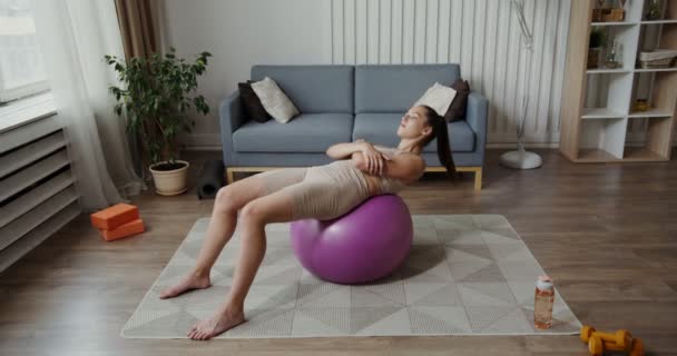 Evropská dívka oblečená ve sportovním oblečení otřese tiskem sedící na gymnastickém míčku — Stock video