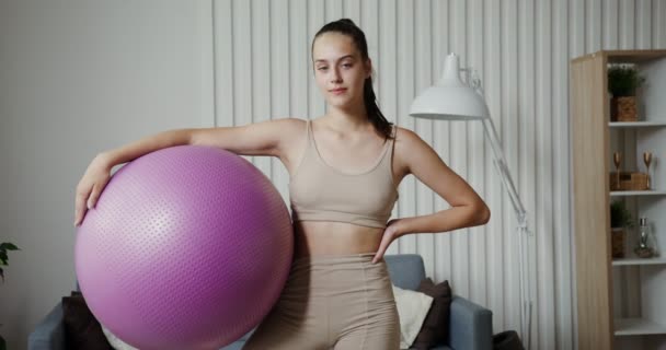 Menina europeia vestida de sportswear fica com uma bola de ginástica em suas mãos — Vídeo de Stock