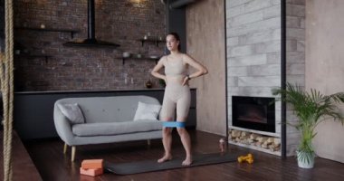 Spor kıyafetleri giymiş Avrupalı bir kız jimnastik lastiğiyle egzersiz yapıyor.