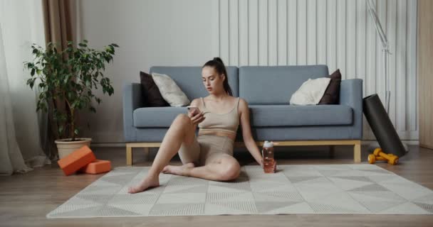 European girl dressed in sportswear sitting on the floor using the phone — Stock Video