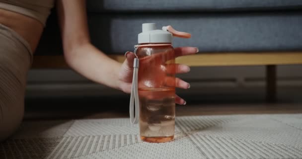 Une fille à la peau claire prend une bouteille d'eau de sport debout sur le sol — Video