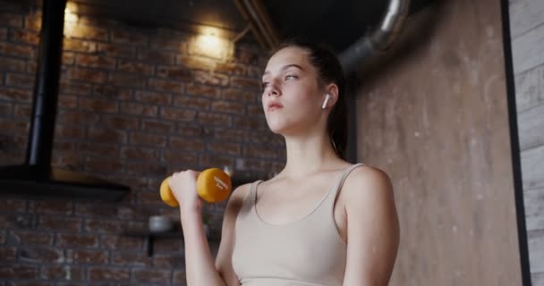 Spor kıyafetleri giymiş Avrupalı bir kız dambıllarla egzersiz yapıyor. — Stok video