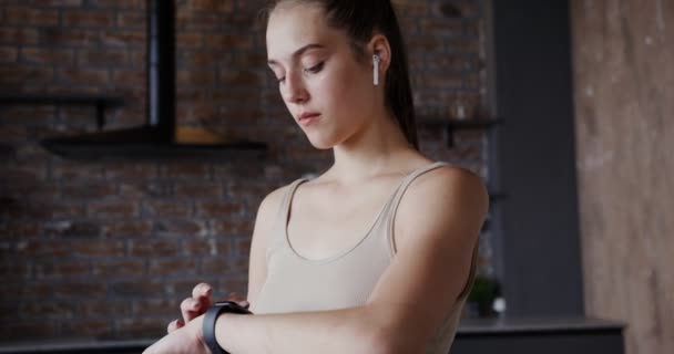 Chica europea vestida con ropa deportiva utiliza un reloj inteligente o pulsera de fitness — Vídeos de Stock